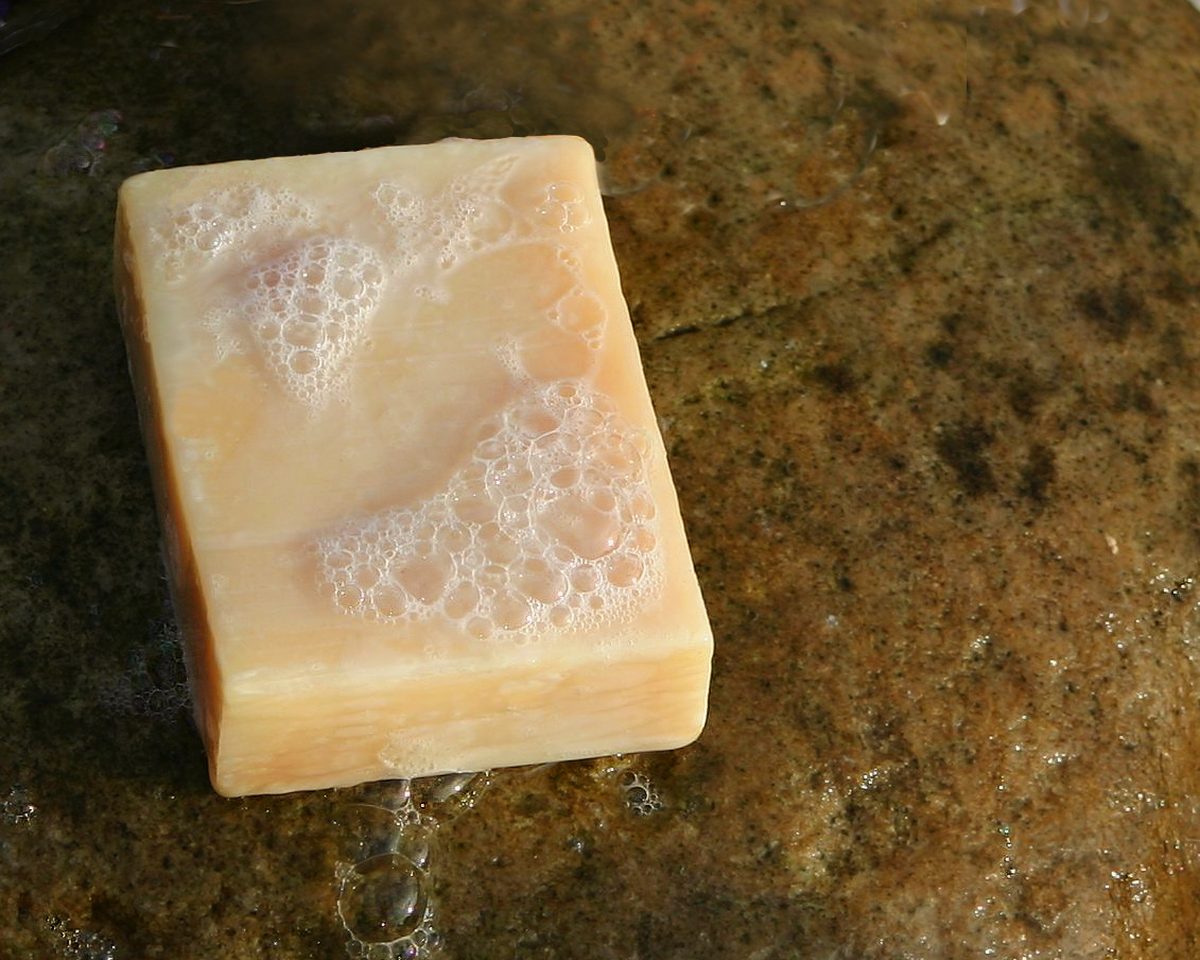 Un panetto di sapone chiaro appena tagliato su un tagliere di legno, con una spatola accanto